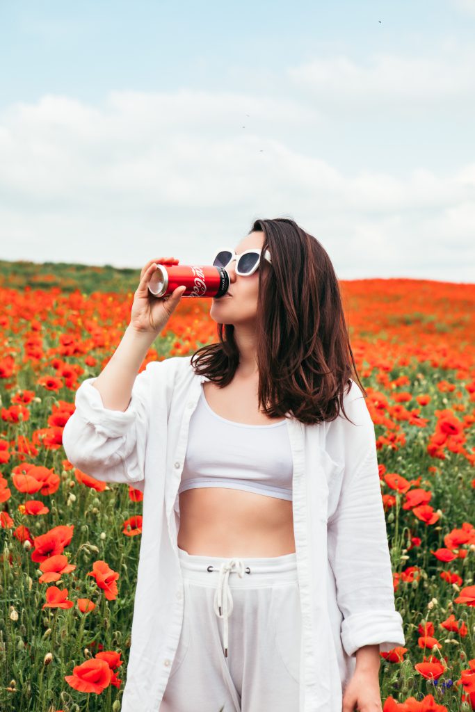 Lviv, Ukraine Jun 11, 2020: Woman Drinking Coca Cola Standing At The Field Of Poppy Flowers. Hot Summer Day